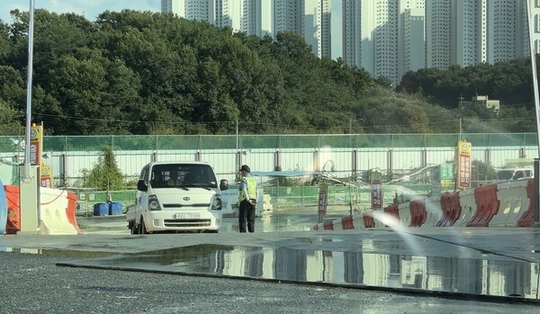 5일 유성구청 환경과 직원의 현장 점검을 앞두고 공사차량이 세륜기를 통과하도록 되돌아가고 있으며, 작업자가 바닥에 물을 뿌려 먼지 발생을 줄이는 모습. [사진= 굿모닝경제 조준영 기자]