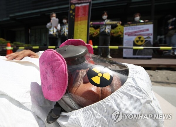 2021년 5월 6일 방호복을 착용하고 방독면을 쓴 한 시위 참가자가 침대 매트리스 위에서 '라돈 피해' 퍼포먼스를 하고 있다. [사진=연합뉴스]